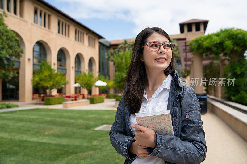 cheerful asian taiwanese female freshman student holding book feeling excited about her school life while sheâs on spring semester study abroad program at school university